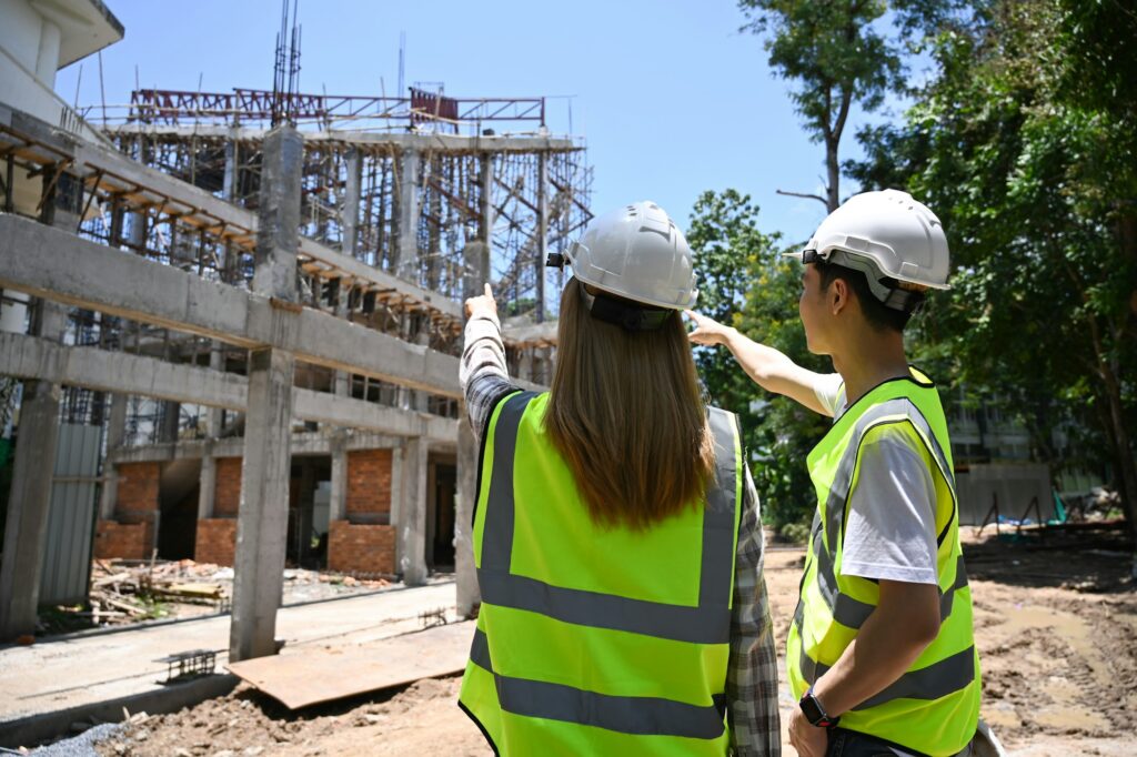 Back view civil engineer discussing, planning development details together at construction site.